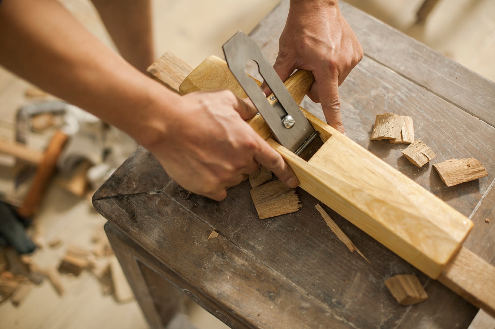 Craftsperson smoothing a wood board with a hand plane.